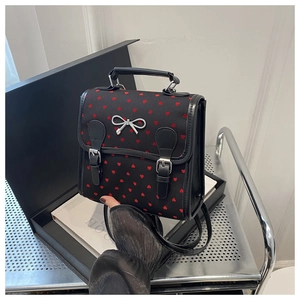 Detail of black backpack with red heart patterns, silver bow, and buckle straps