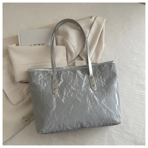 Close-up of silver tote bag with crinkled texture, golden rivets and slim shoulder straps