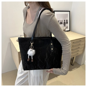 Close-up of black pleated tote bag featuring golden rivets and a white plush charm