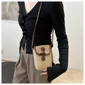 Detail of woven straw phone bag featuring a vintage horn buckle and leather trim