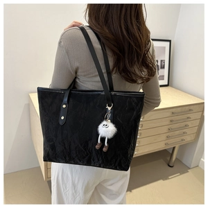 Detail of black tote bag featuring crinkle texture and a white plush doll charm