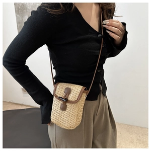 Detail of straw woven phone bag with brown leather trim and classic horn buckle closure