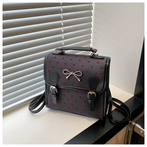 Detail of grey canvas backpack featuring red heart prints and a silver bow ornament