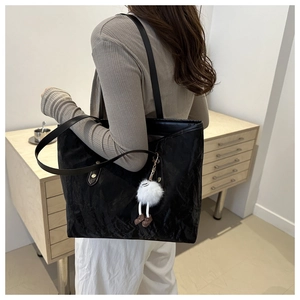 Detail of large black tote bag with textured surface and a cute white plush charm