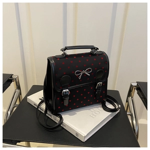 Close-up of black canvas backpack with red heart prints and silver bow detail on a book