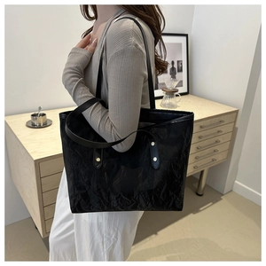 Detail of black wrinkled leather tote bag with gold rivets worn by a model in a minimal room