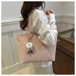 Pink pleated nylon tote bag with plush monster charm worn by a model in a minimalist room