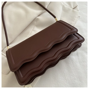 Détail d'un sac porté épaule marron foncé avec bord festonné et détails dorés