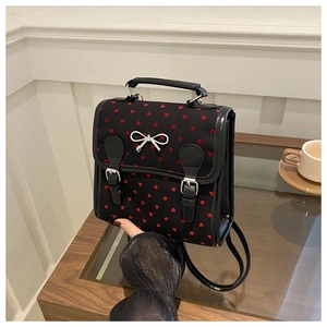 Detail of black backpack with red heart patterns and silver metal bow on a wooden desk