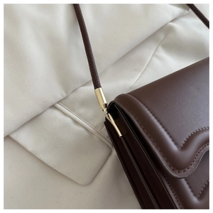 Détail du sac bandoulière marron foncé avec coutures ondulées et ferrures dorées