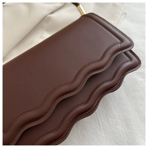 Détail du sac en cuir marron foncé avec bord ondulé et finitions métalliques dorées