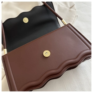 Détail du sac à bandoulière marron avec bordure festonnée et fermoir magnétique doré