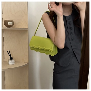 Détail du sac à bandoulière vert vif avec un rabat ondulé unique et une texture en cuir fin
