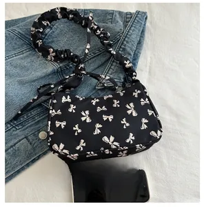 Close-up of black nylon underarm bag with white bow print and ruffled cloud strap