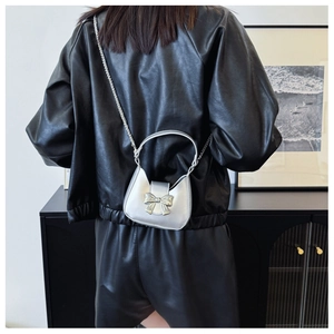 Close-up of a mini silver metallic half-moon bag with a bow detail and silver chain strap