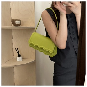 Detail of avocado green baguette bag with wavy edge design and gold metal accents