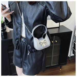 Silver mini crossbody bag with metal bow detail and chain strap worn by model