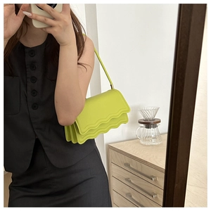 Chic neon green shoulder bag with wave flap design worn by a model in a casual setting