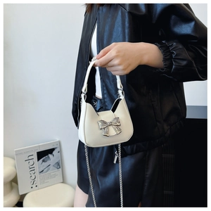 Detail of white mini handbag featuring a large silver bow and elegant metal chain strap