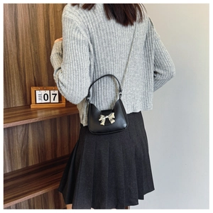 Mini black leather crossbody bag with silver bow accent and chain strap worn by a model