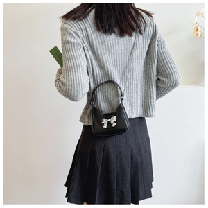 Close-up of black crescent crossbody bag with silver bow buckle and delicate metal chain