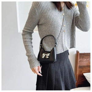 Detailed close-up of a mini black leather crossbody bag with a silver metallic bow accent