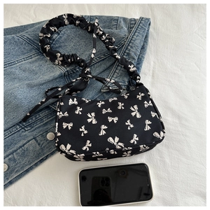 Detail of black nylon underarm bag with white bow print and ruffled cloud shoulder strap