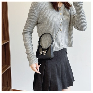 Detailed shot of black mini bag with large silver bow buckle and chain strap on a model