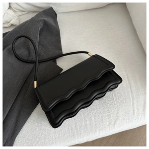 Dettaglio borsa a tracolla minimalista in pelle nera con bordo ondulato e fibbie dorate