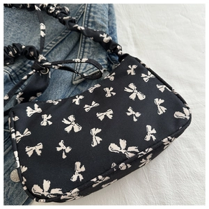 Close-up of black canvas underarm bag featuring white bow prints and ruched shoulder strap