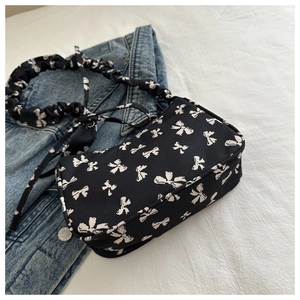 Close-up of black nylon underarm bag featuring white bow prints and ruffled shoulder strap