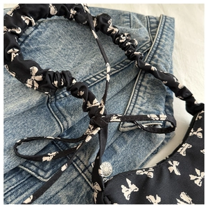 Detail of black nylon underarm bag with white bow patterns and pleated ruffle strap