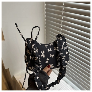 Detail of black nylon underarm bag featuring white bow patterns and ruched cloud handle