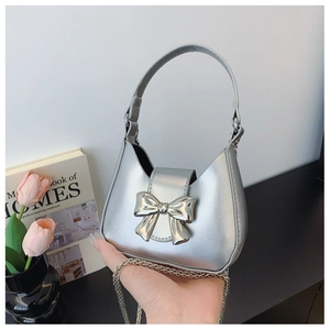 Detail view of mini silver crescent bag featuring a large metal bow and thin chain strap