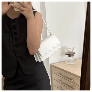 Detailed view of white crossbody bag featuring triple-layered scalloped edge flap and gold hardware