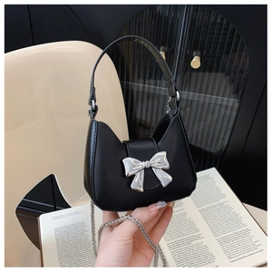 Close-up of a mini black half-moon handbag with a silver bow clasp and metal chain