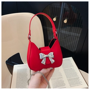 Detail of red leather mini bag with a silver mirror bow and chain strap on a book