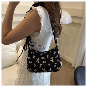 Detail of black nylon underarm bag featuring white bow patterns on model shoulder