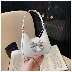 White mini handbag with silver bow detail and chain strap on an open book