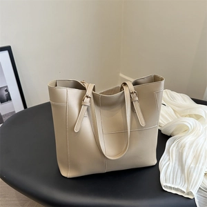 Minimalist beige oversized tote bag with adjustable straps on a sleek black pedestal