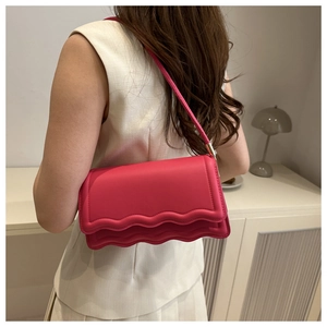Detail view of pink shoulder bag with wavy edge design worn by a model in casual setting