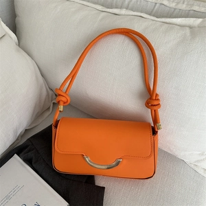 Orangefarbene Baguette-Tasche mit goldener Schnalle und Knotengurt auf einem Blazer-Hintergrund