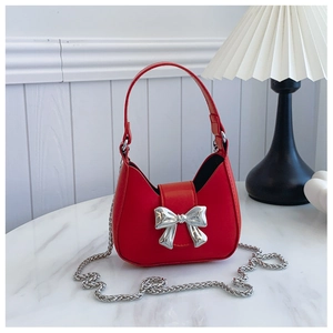 Detail of red crescent handbag featuring a silver metal bow and detachable chain strap