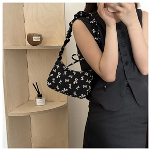 Detail of black underarm bag featuring white bow prints and ruffled ruched shoulder strap