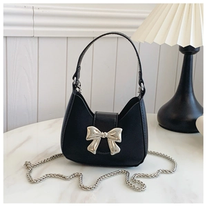 Detail of mini black crossbody bag featuring silver bow buckle and delicate chain strap