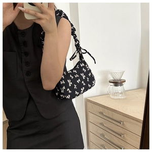 Close-up of a black nylon shoulder bag with white bow prints and ruched strap detail