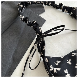 Close-up of black canvas shoulder bag with white bow print and pleated cloud strap detail