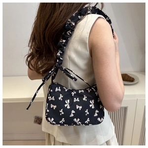 Close-up of black canvas shoulder bag with white bow prints and ruffled strap detail