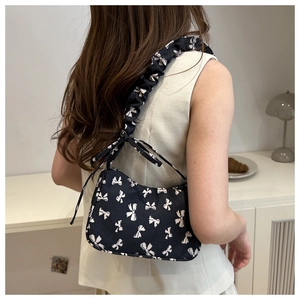 Detail of black shoulder bag with white bow pattern and ruffled strap on a model