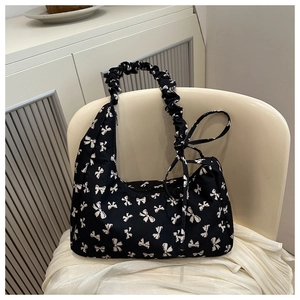 Black hobo bag with white bow pattern and ruched handle on a minimalist chair